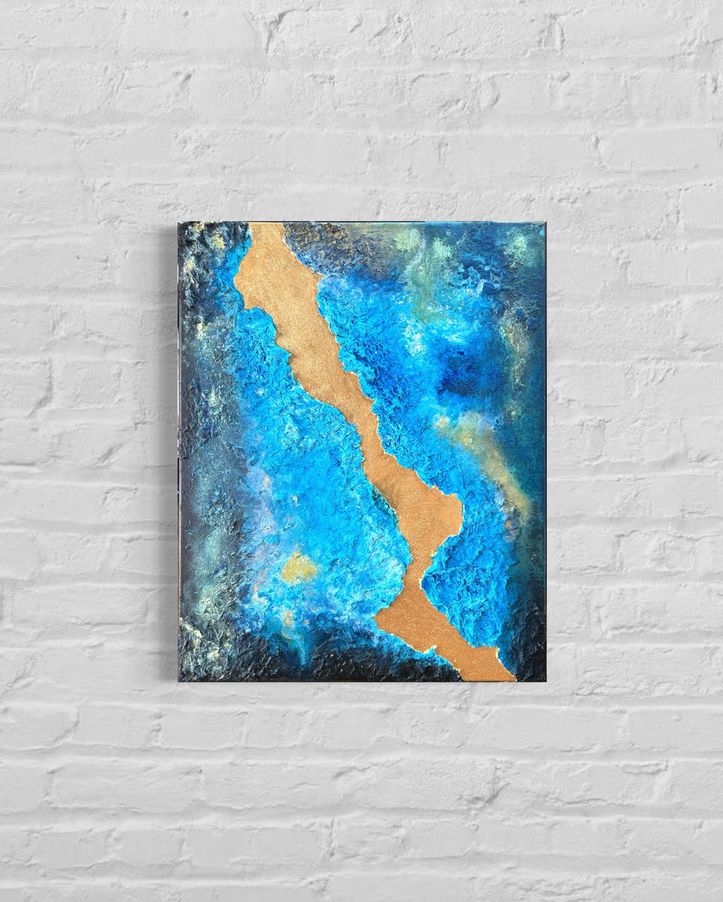 Abstract painting with blue and gold on a white brick wall
