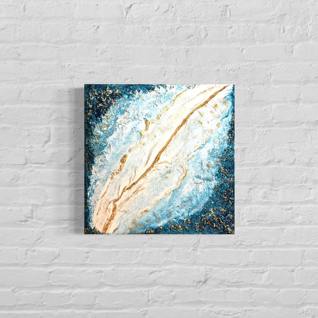 Abstract painting with blue, gold, and white on a white brick wall