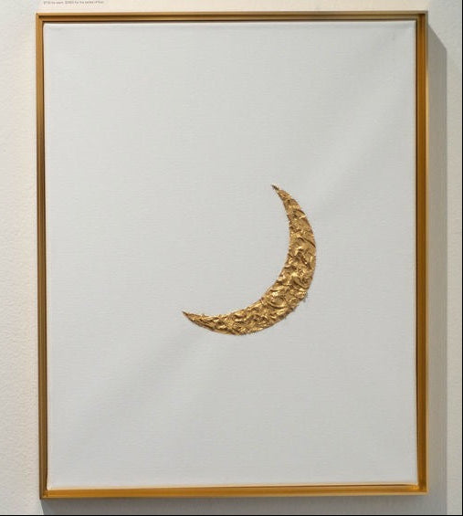 Gold crescent moon sculpture in a gold frame on a white wall