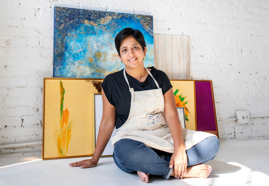 Anshu, the artist sitting in front of paintings and textured white wall